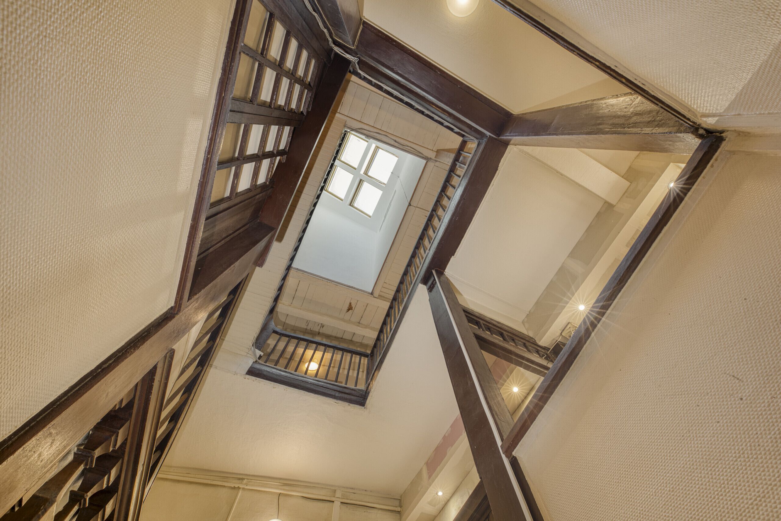 Un escalier à haute plafond, doté de rampes en bois et d’une lucarne.