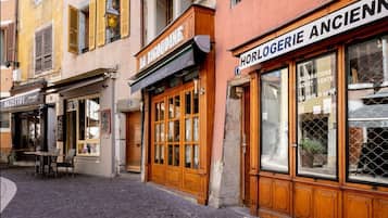 Une vue de rue avec un restaurant appelé « LA BIGOUINE » et un magasin appelé « HORLOGERIE ANCIENNE ».