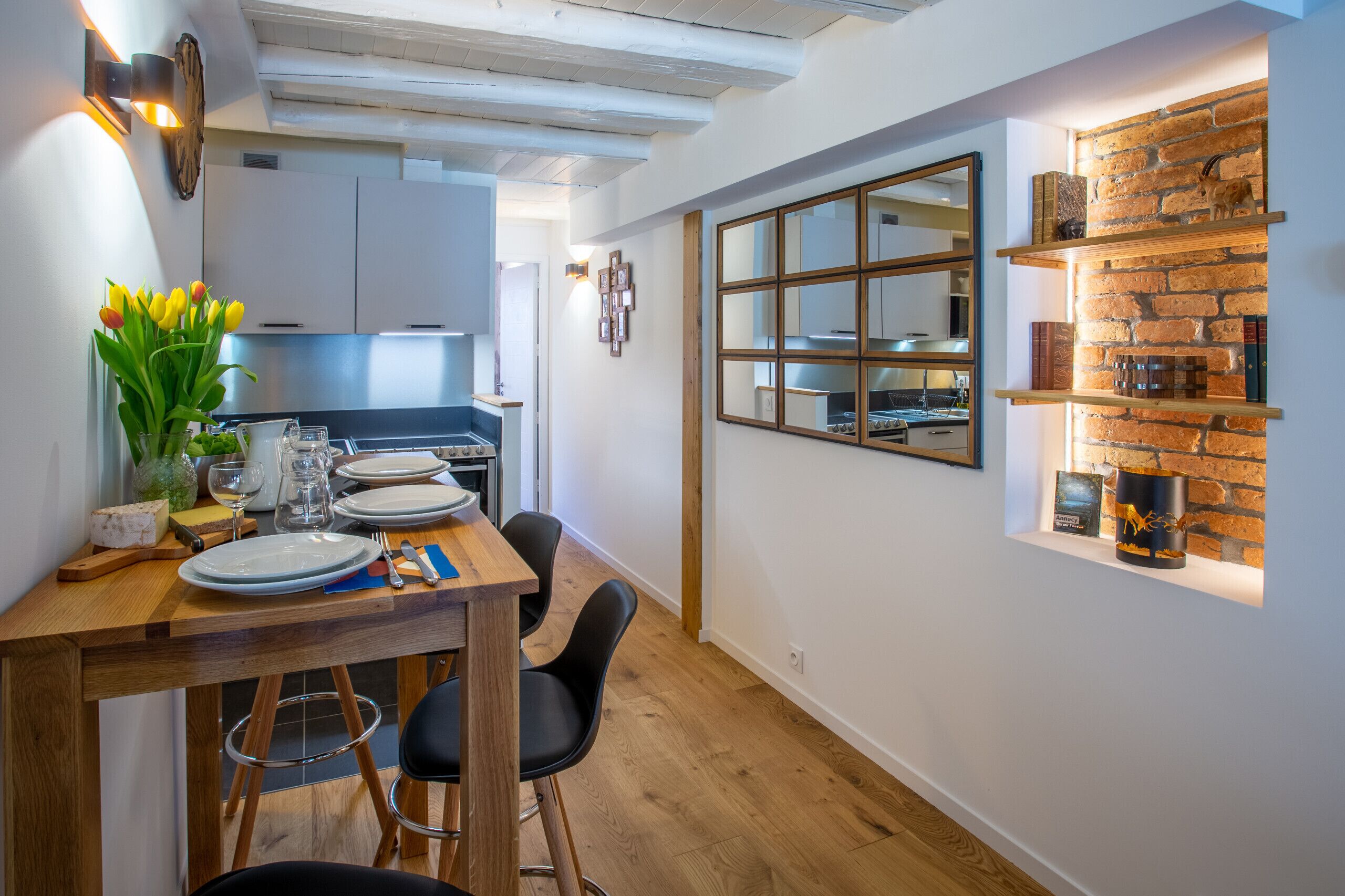 A modern kitchen with a dining area, wooden flooring, and a brick accent wall.