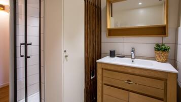 A modern bathroom with a glass shower enclosure, a wooden vanity with a mirror, and a small potted plant.
