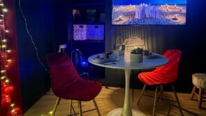 Ein Zimmer mit einem runden Tisch, zwei roten Stühlen, einer kleinen Lampe und einem Fernseher, der eine Strandansicht zeigt.