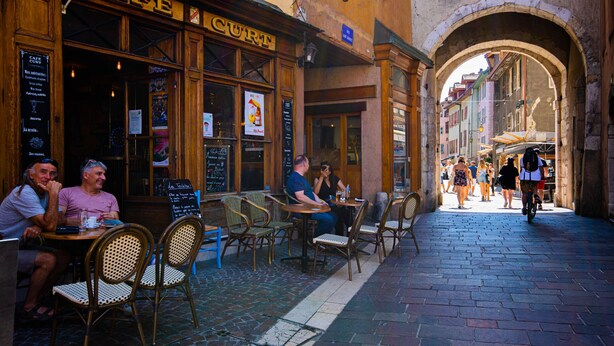 Ein Café mit Außenbestuhlung, Holzmöbeln und einem Kopfsteinpflasterweg.