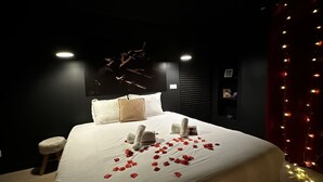 Ein ordentlich bezogenes Bett mit weißen Leinentüchern und Rosenblättern, ein kleiner Hocker und ein an der Wand befestigtes Regal mit einem gerahmten Bild.