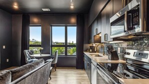 A modern kitchen with a built-in microwave, oven, and sink. There is a seating area with a sofa and chairs near a large window.