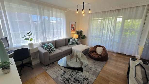 Een moderne woonkamer met een grijze bank, een glazen salontafel, een bruine relaxfauteuil en een bureau met een computer.
