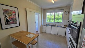 Een keuken met witte kasten, een raam met uitzicht op groen en een klok aan de muur.