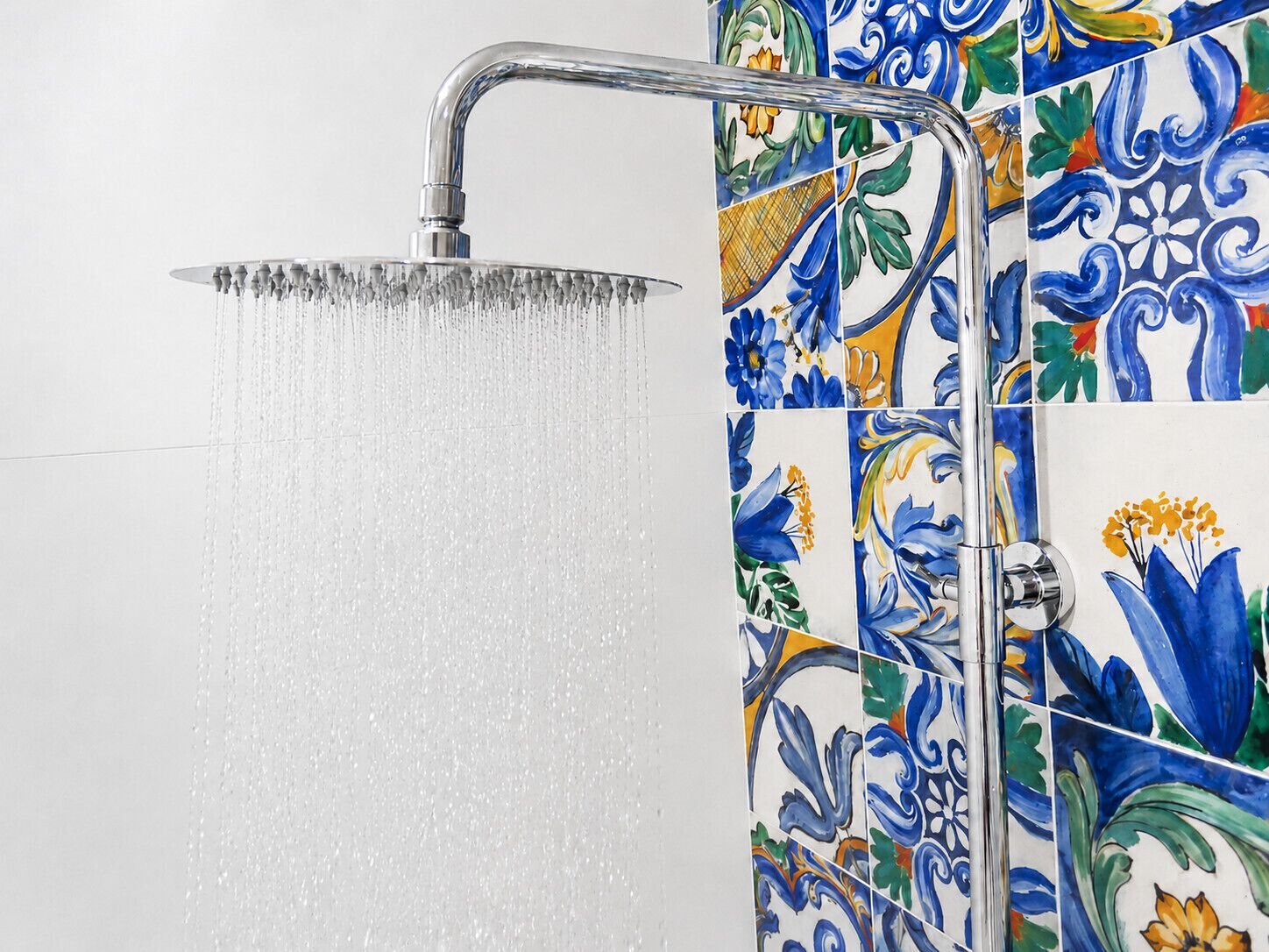 Een douche met stromend water, een metalen kraan en een betegelde muur met bloemmotieven.