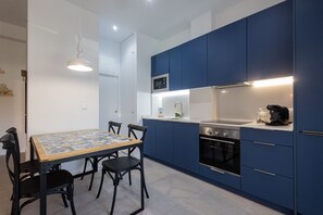 A compact kitchen with blue cabinets, a microwave, a stove, and a coffee maker.