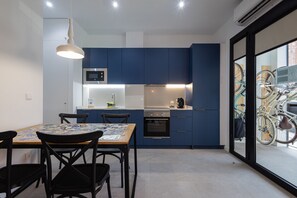 Eine moderne Küche mit blauen Schränken, einer Mikrowelle und einem Herd. Ein Esstisch mit Stühlen und ein Fenster, vor dem Fahrräder stehen.