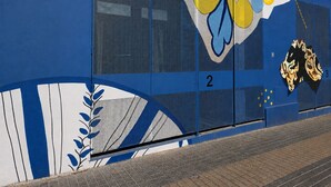 Un edificio con fachada azul, un ventanal con mosquitera y un mural colorido.
