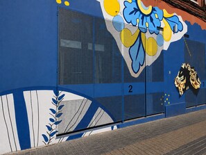 A building with a blue exterior, a large window with a mesh screen, and a colorful mural.