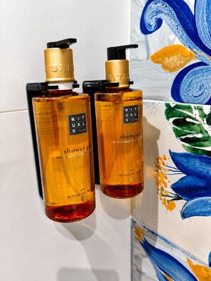 Deux bouteilles de gel douche Rituals sont posées contre un mur carrelé, sur lequel on aperçoit une peinture abstraite aux tons bleus et blancs.