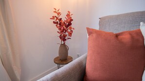 Esquina de una habitación con un sofá gris, una mesita de madera y un jarrón con hojas rojas.