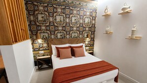 Habitación de hotel con una cama grande, una mesita de noche, un cabecero de madera, un tapiz estampado y un estante de pared con adornos.