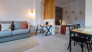 Un salon moderne avec un canapé gris, un mur d’accent en bois, une table à manger avec des chaises et un petit bureau avec un ordinateur portable.
