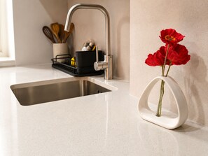 Un lavamanos de cocina con un grifo moderno, un portalapices y un florero con flores rojas en la encimera.