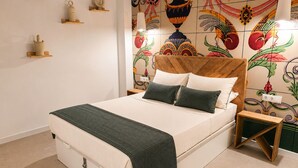 Un lit avec une tête de lit en bois, deux oreillers, un plaid vert et une table de chevet avec une lampe.