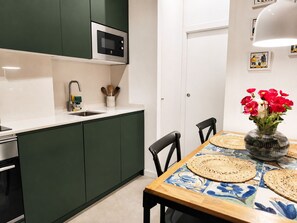 Une cuisine moderne avec des meubles de couleur verte, un four à micro-ondes et un évier. On y trouve une table à manger ornée d’un vase de fleurs rouges et de sets de table en fibres tressées.