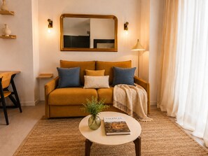 A living room with a sofa, a coffee table with a book, a vase with plants, and a lamp.