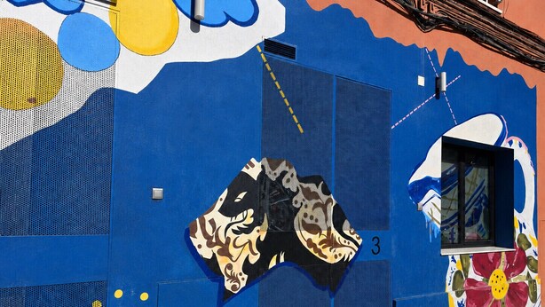 Un bâtiment à la façade bleue, une fenêtre ornée d’une fresque colorée et le chiffre « 3 » peint sur le mur.