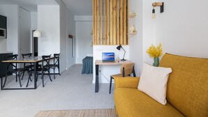 A modern living room with a sofa, a dining table with chairs, a laptop on a desk, and a wooden slat wall panel.