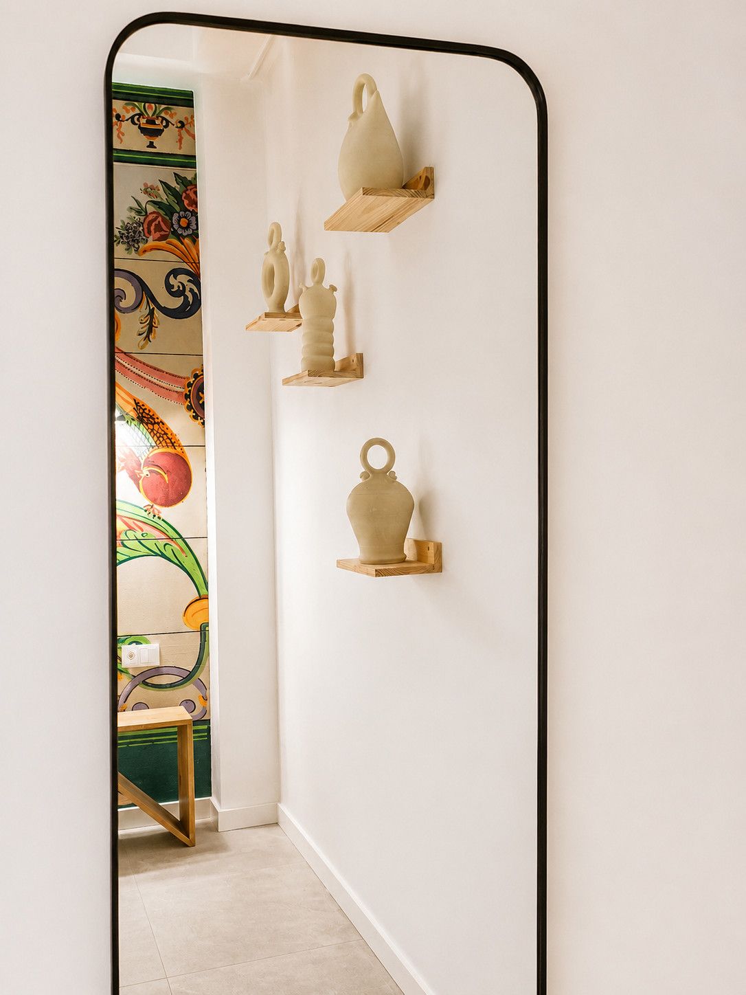 A hallway with a mirror reflecting a wall-mounted shelf holding ceramic vases.