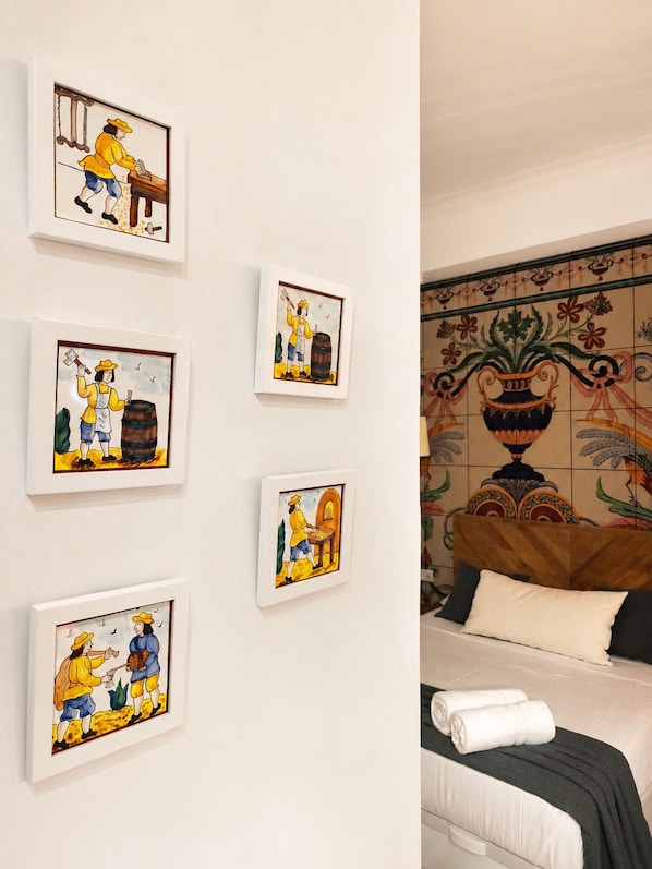 A hotel room with a bed, a wall with framed artwork, and a decorative tile wall.