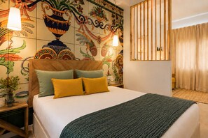 Habitación de hotel con cama, un adorno en la pared, cabecero de madera, mesita de noche y una ventana con cortinas.