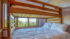 A bunk bed with a wooden frame and a view of greenery through the window.