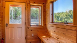 A wooden cabin interior with a bench, two windows, and a door.