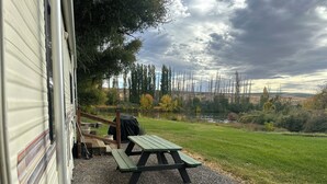 Mesa de picnic cubierta y zona de barbacoa junto a una casa móvil sobre suelo de grava.