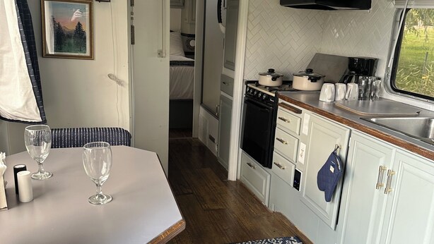 Una cocina compacta con estufa, horno y lavadero, un comedor con mesa y sillas, y un tapete estampado.