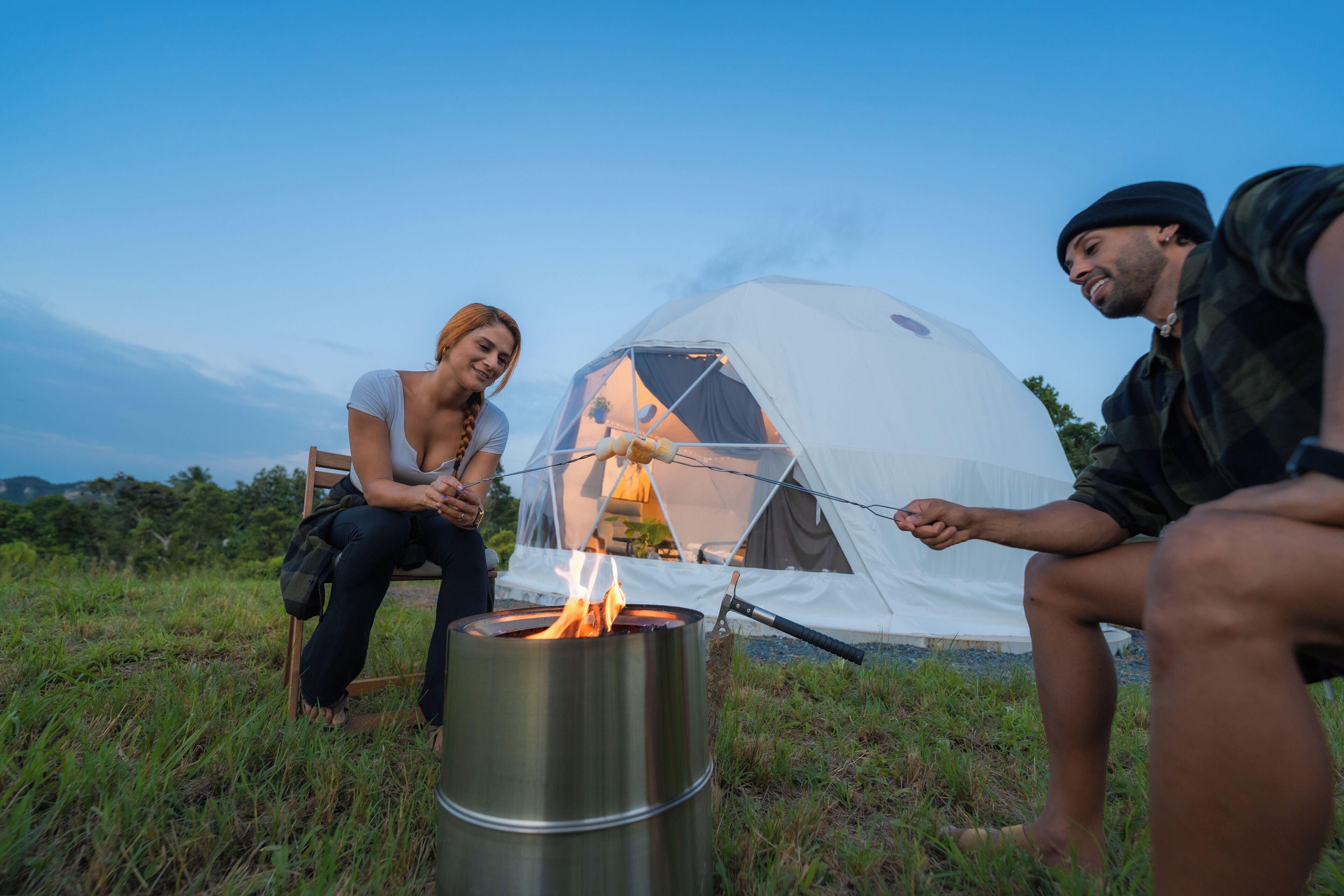 A group of people around a campfire with a tent in the background.