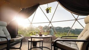 Een gezellig interieur met een ronde tafel, twee stoelen en uitzicht op een bergachtig landschap door een geometrisch raam.