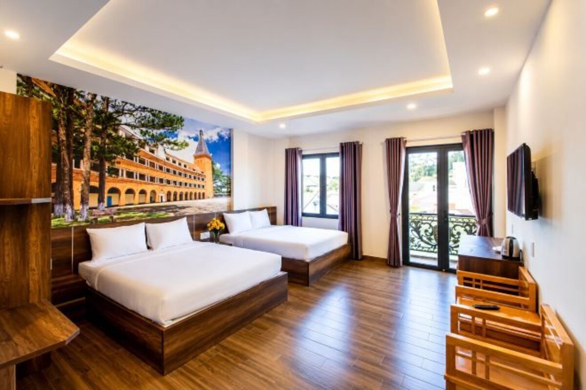 A hotel room with two beds, a wooden floor, a mural, and a balcony with curtains.