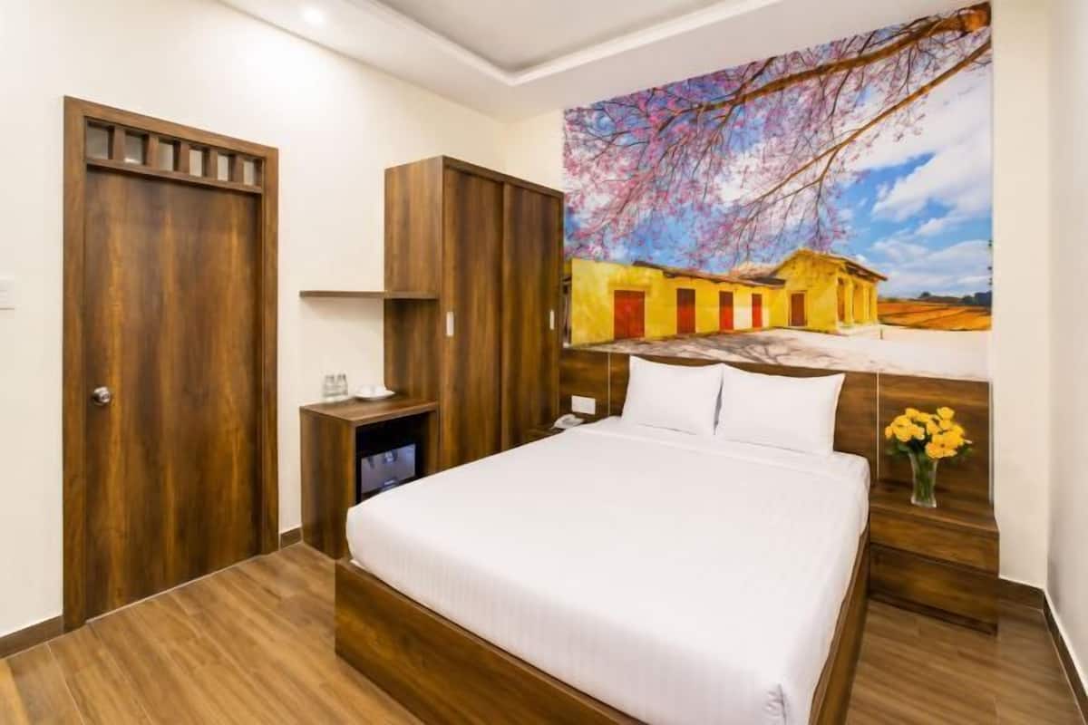A bedroom with a bed, wooden wardrobe, nightstand, and a painting on the wall.