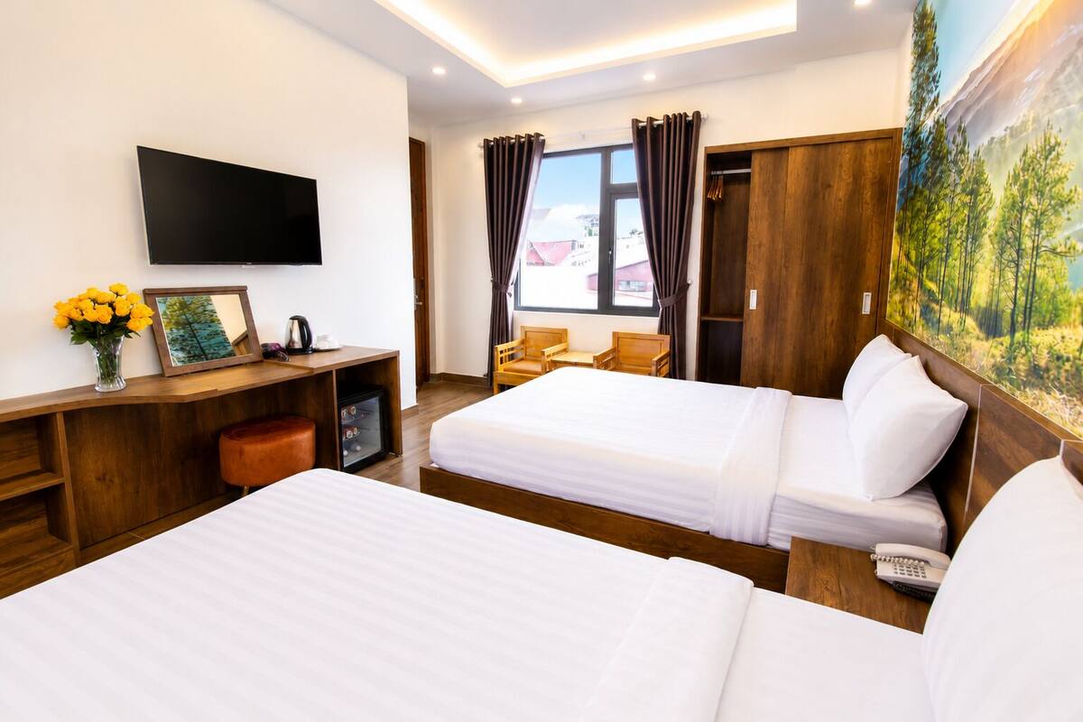 A hotel room with two beds, a TV, a desk with a chair, a small fridge, and a painting on the wall.
