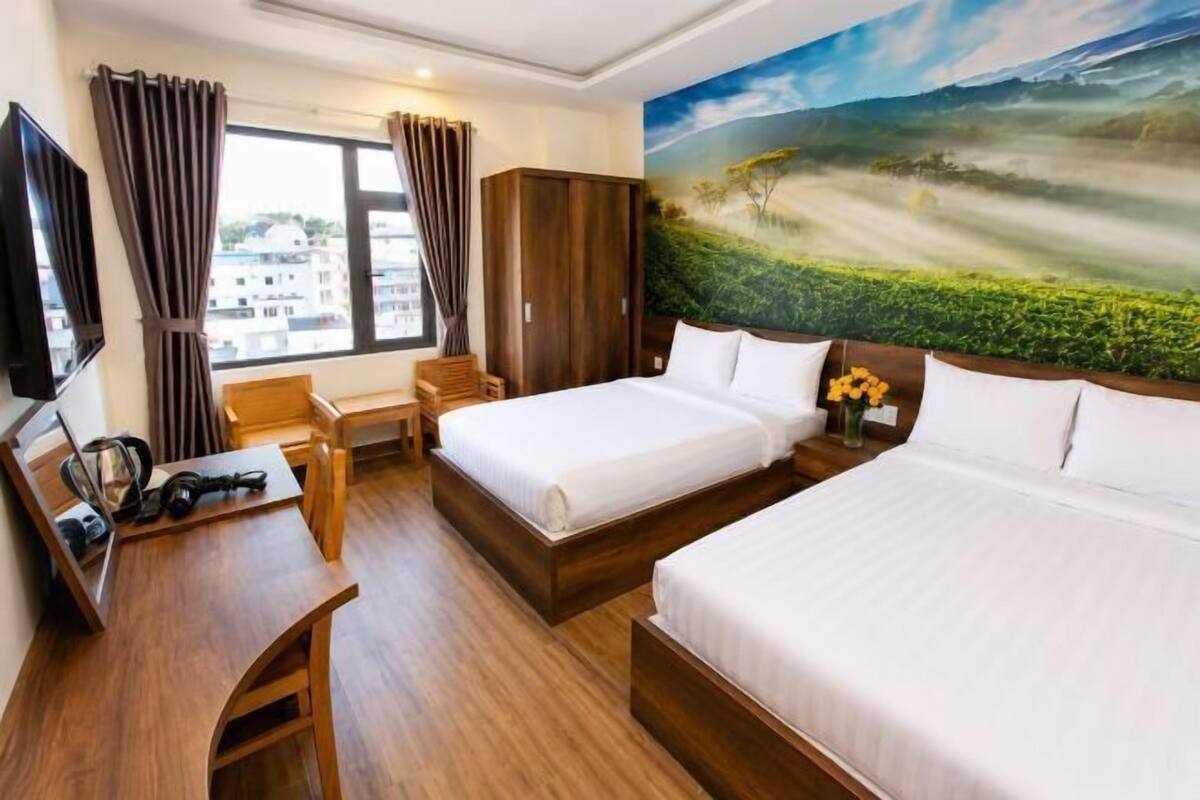A hotel room with two beds, a desk, a chair, a TV, and a painting of a landscape.