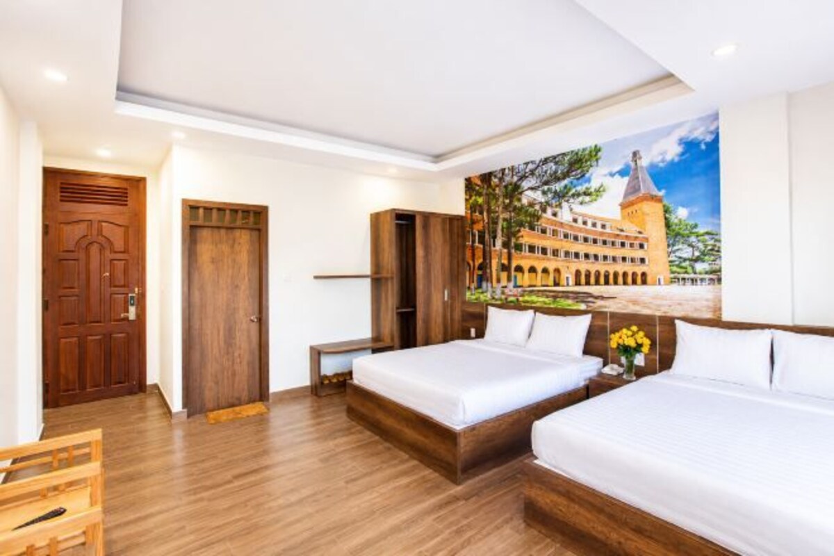 A hotel room with two beds, a wooden wardrobe, a desk, and a mural of a building.