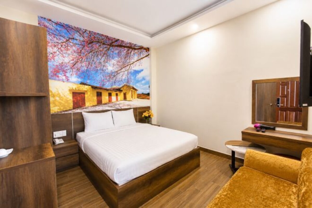 A hotel room with a bed, a TV, a wooden desk, and a large painting on the wall.