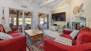 A spacious living room with red sofas, a wooden coffee table, and a patterned rug. There is a television, a lamp, and a decorative fish wall art piece. - Lake Home with Private Beach and Hot Tub (Ossipee)