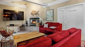 A living room with a fireplace, red sofas, a wooden coffee table, and a flat-screen TV. - Lake Home with Private Beach and Hot Tub (Ossipee)