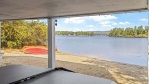 A covered outdoor area with a view of a lake, a sandy beach, and a red circular object. - Lake Home with Private Beach and Hot Tub (Ossipee)