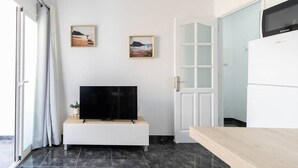 Un salon moderne avec un téléviseur à écran plat posé sur une console blanche, deux tableaux encadrés accrochés au mur et une porte-fenêtre coulissante donnant sur un balcon.