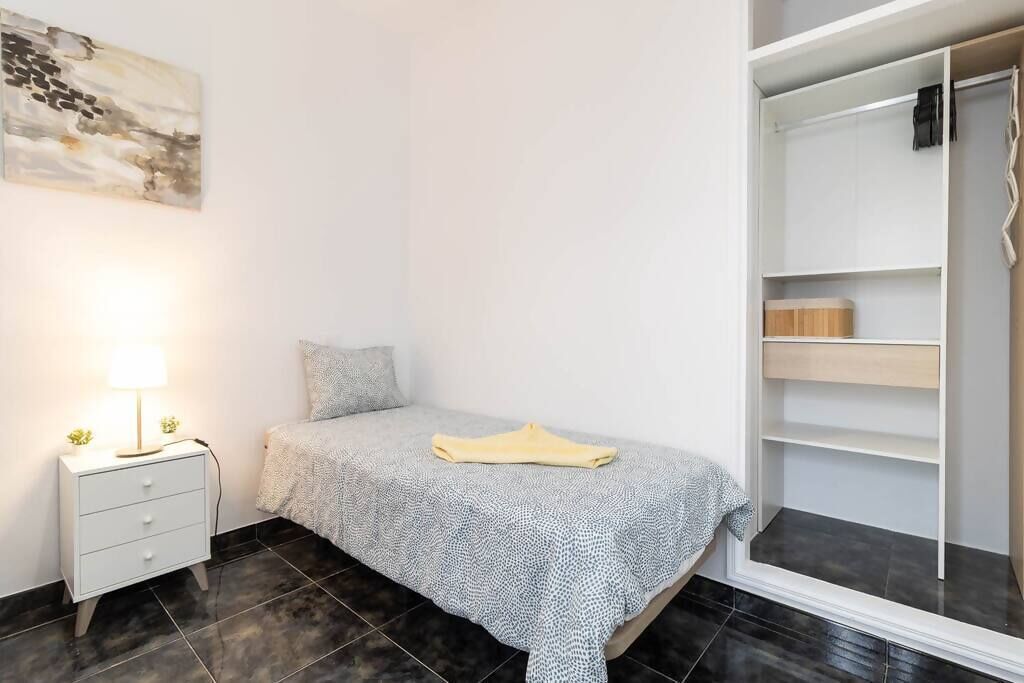A bedroom with a bed, a nightstand with a lamp, a closet, and a wall-mounted artwork.