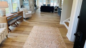 A spacious living area with a wooden floor, a large rug, and a seating area with a bench and chairs.