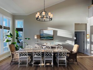 A dining area with a wooden table and chairs, a chandelier, and a large window with plants.