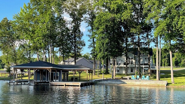 A lakeside building with a covered dock and a grassy area with chairs.