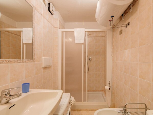 Une salle de bain équipée d’un lavabo, d’un miroir, d’un porte-serviettes, d’une douche et de toilettes.