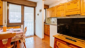 A kitchen with wooden cabinets, a TV, and a dining area with a table and chairs. - Apartment Apt 18 by Interhome (Canazei)